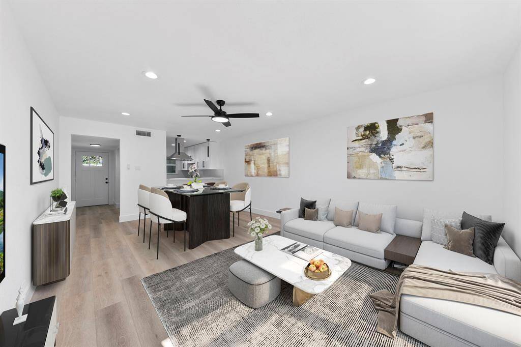 This photo showcases a modern open-concept living and dining area. The space features light wood flooring, a cozy sectional sofa, and a stylish dining table. Contemporary artwork and sleek furniture create an inviting atmosphere. Recessed lighting and a ceiling fan add to the room's appeal, making it perfect for entertaining or relaxing.