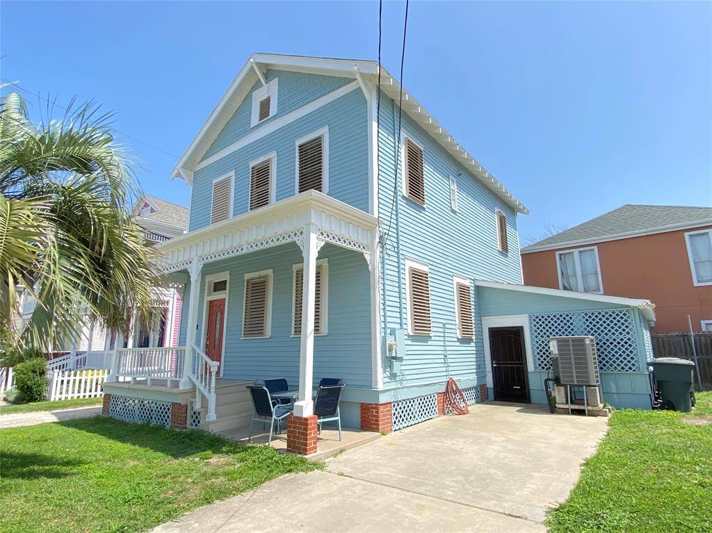 Charming two-story blue home with a welcoming front porch, featuring decorative white trim and shutters. The property includes a driveway and a small yard with a palm tree, offering a coastal vibe and curb appeal.