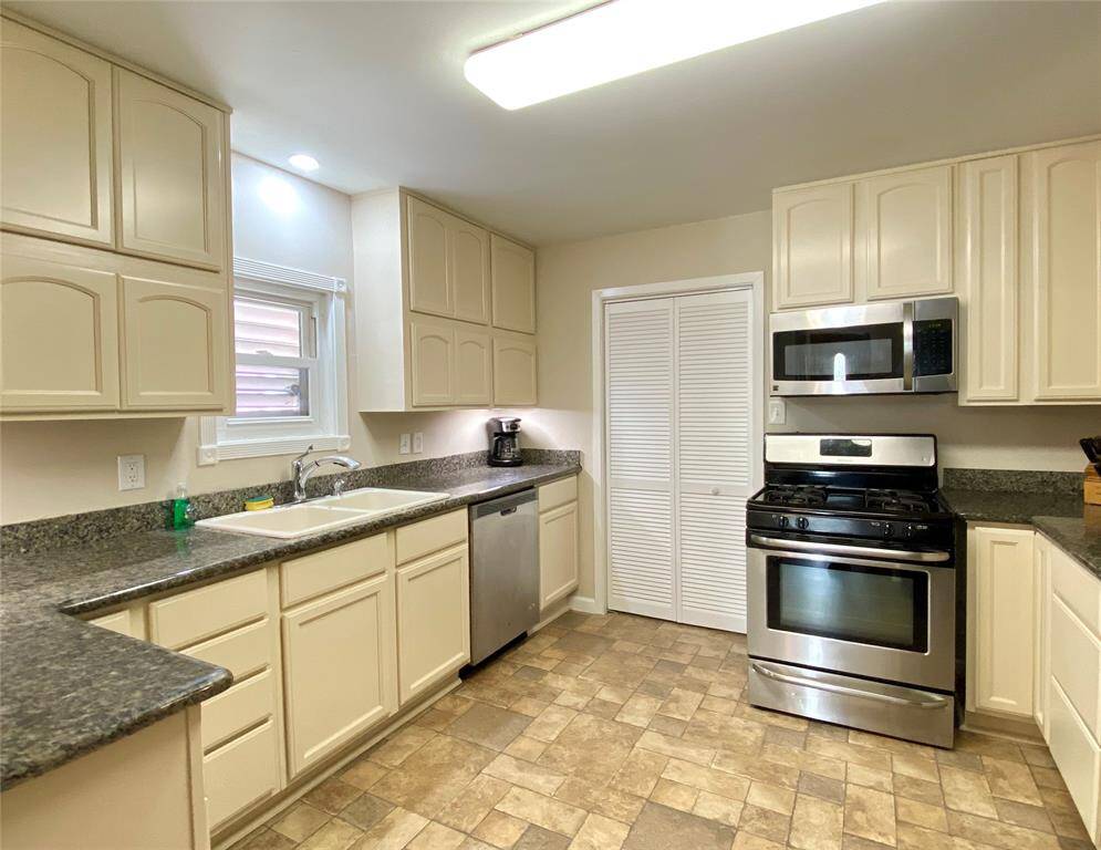 Bright, spacious kitchen with modern stainless steel appliances, ample cabinetry, and sleek granite countertops. Features a gas stove, dishwasher, and a double sink under a window.