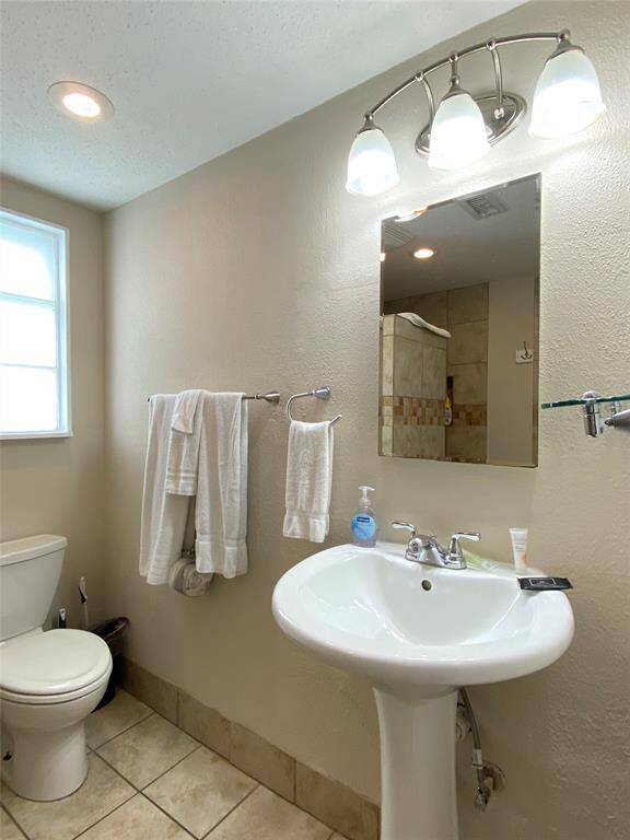 This is a bright bathroom featuring a pedestal sink, modern lighting, and a tiled shower. It has neutral walls, a window for natural light, and a convenient towel rack.