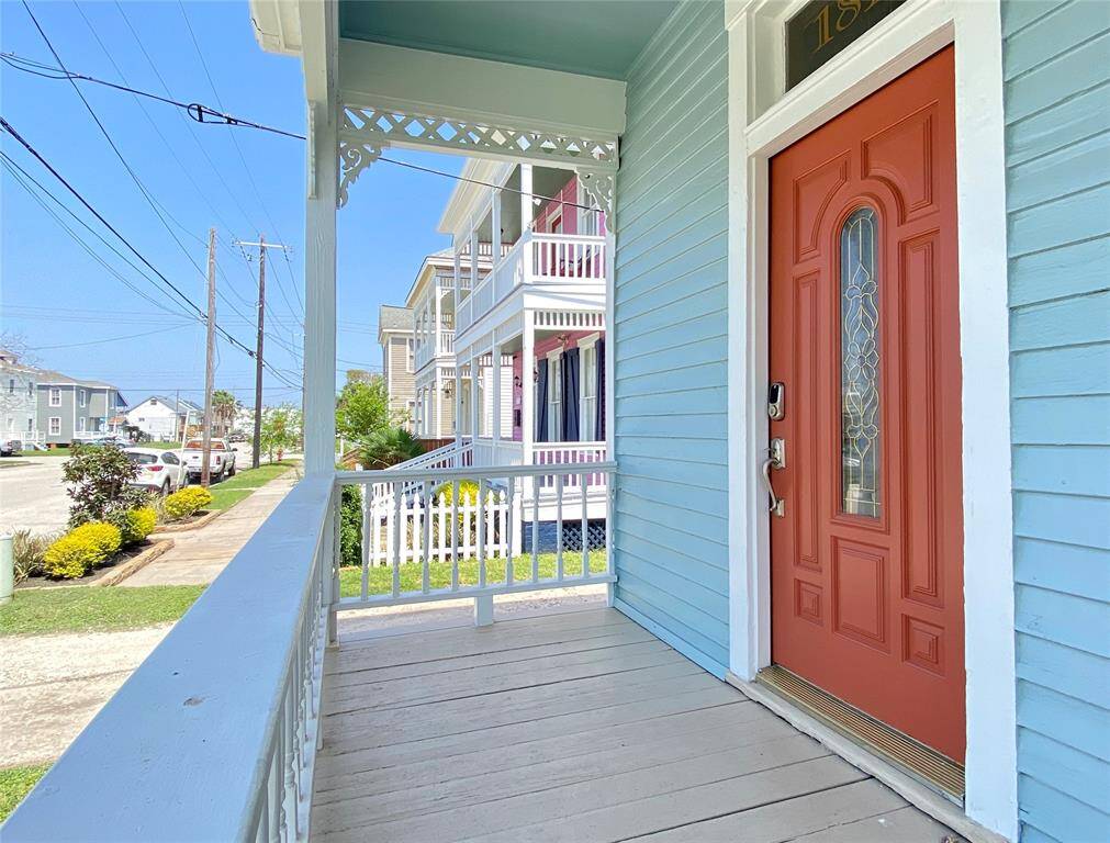 Charming front porch with a decorative red door and intricate detailing on a light blue house. The neighborhood features well-maintained homes and manicured lawns, creating a welcoming street view.