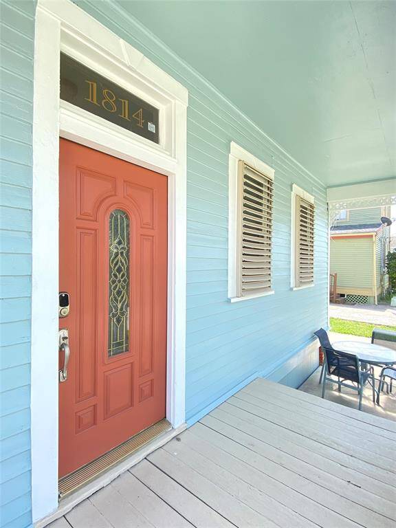 Charming front porch with a bold red door and decorative glass. The porch is painted a light blue, featuring two shuttered windows and space for outdoor seating.