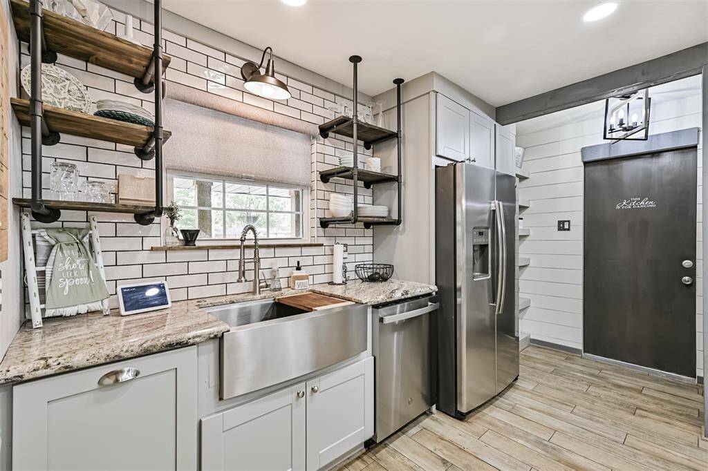 The kitchen features industrial open shelving, a stylish stainless steel apron sink, and a sleek tile backsplash—creating a functional and visually striking design that’s perfect for both everyday use and entertaining.