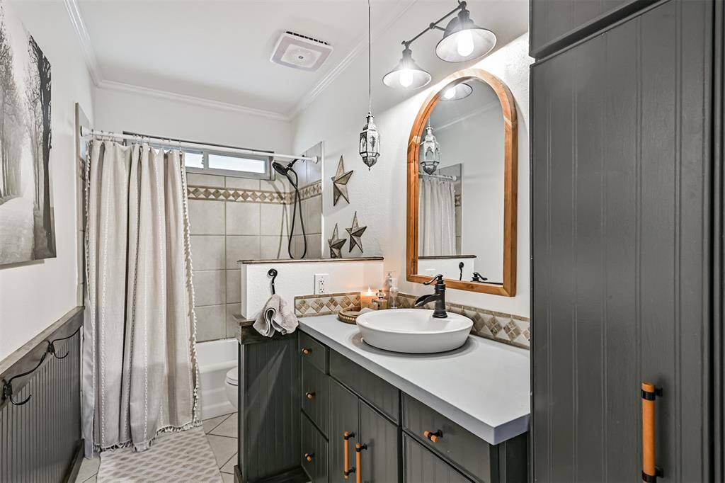 Secondary bathroom feature stylish Urban Bronze cabinets, accented with beadboard and a custom stained-wood ledge with hooks. All faucets and fixtures have been upgraded to sleek black, complemented by updated lighting and mirrors, creating a modern, cohesive look throughout each space.