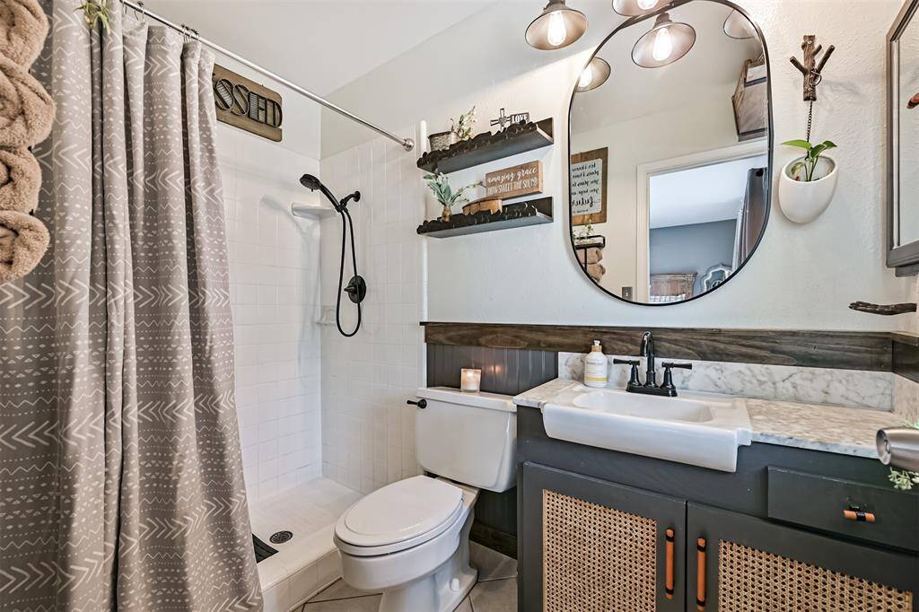 The primary bathroom showcases a custom Urban Bronze vanity, beadboard detailing, and a handcrafted stained-wood ledge with hooks. Upgraded black faucets and fixtures are paired with an oval black-rim mirror and elevated lighting, creating a stylish and cohesive space.