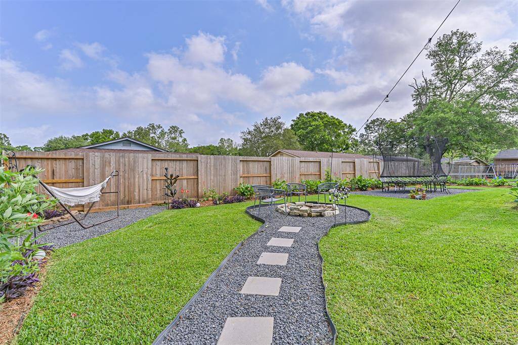 A fire pit is nestled within the black gravel pathway, offering a cozy gathering spot that blends seamlessly into the backyard’s natural landscape—perfect for cool evenings and casual entertaining.