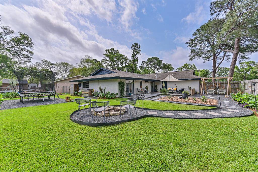 This view of the backyard showcases a beautifully landscaped oasis with river rock accents, a stepping stone path, and a private retreat feel, complete with a fire pit and string lights for a tranquil, inviting atmosphere.