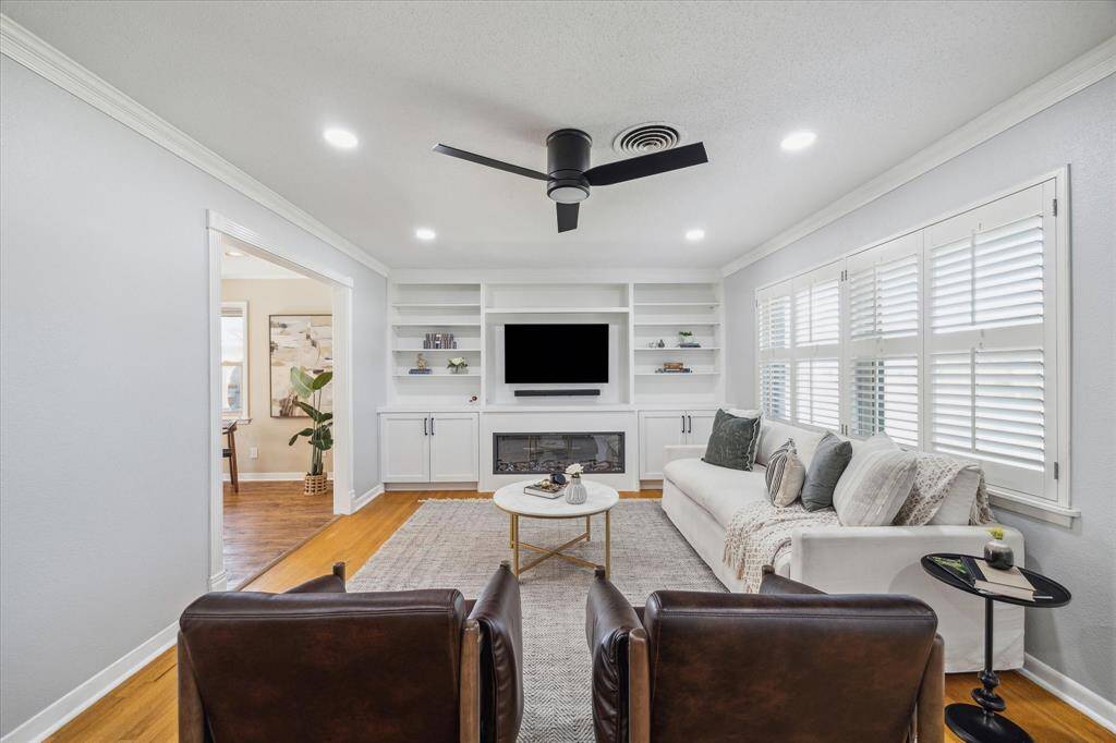 The front door to the home leads to a sizable living room large with original hardwood floors, crown moulding, new built-ins, electric fireplace, and large windows with wood plantation-style shutters.