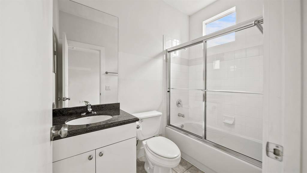 The en-suite bathroom for the secondary third-floor bedroom boasts a granite countertop and a shower with a tub and sleek glass sliding door.