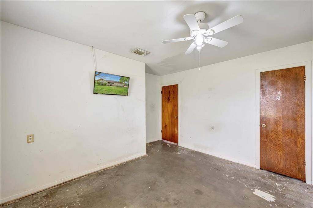 A small, unfinished room with white walls, a ceiling fan, and two wooden doors. The floor is bare, showing some wear. Ideal for customization or renovation.