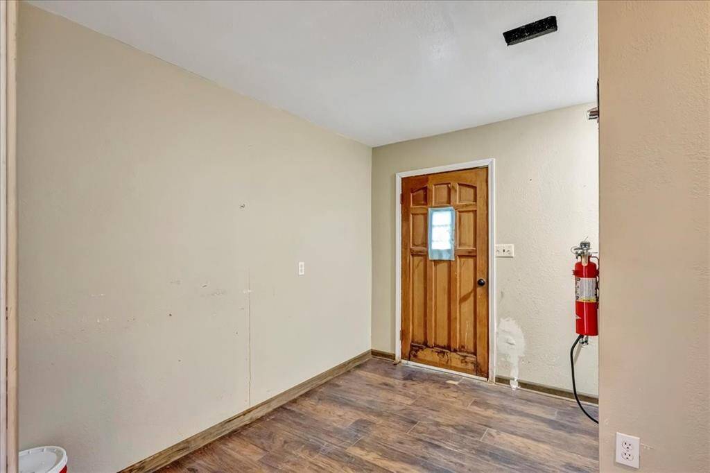This room features a wooden floor and a wooden door with a small window. The walls are painted a neutral color, and there's a fire extinguisher mounted on one wall. It offers a simple, functional space.