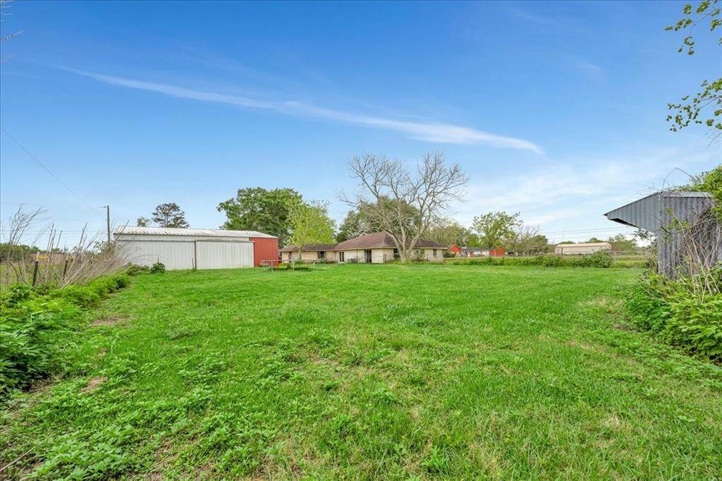 Spacious property with a large grassy yard, featuring a house and multiple outbuildings against a clear blue sky. Ideal for those seeking ample outdoor space.