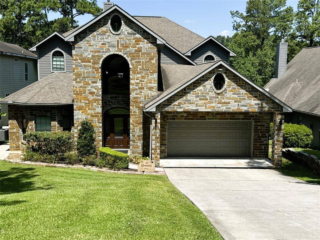 Charming stone-front home with a welcoming entrance and spacious two-car garage, nestled in a lush, green setting.