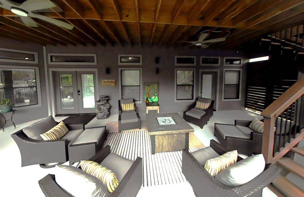 This photo showcases a cozy, covered patio with comfortable wicker furniture and striped cushions, centered around a stylish fire pit table. The space features a wooden ceiling with fans, large windows, and doors leading inside, creating an inviting outdoor living area perfect for relaxation and entertaining.