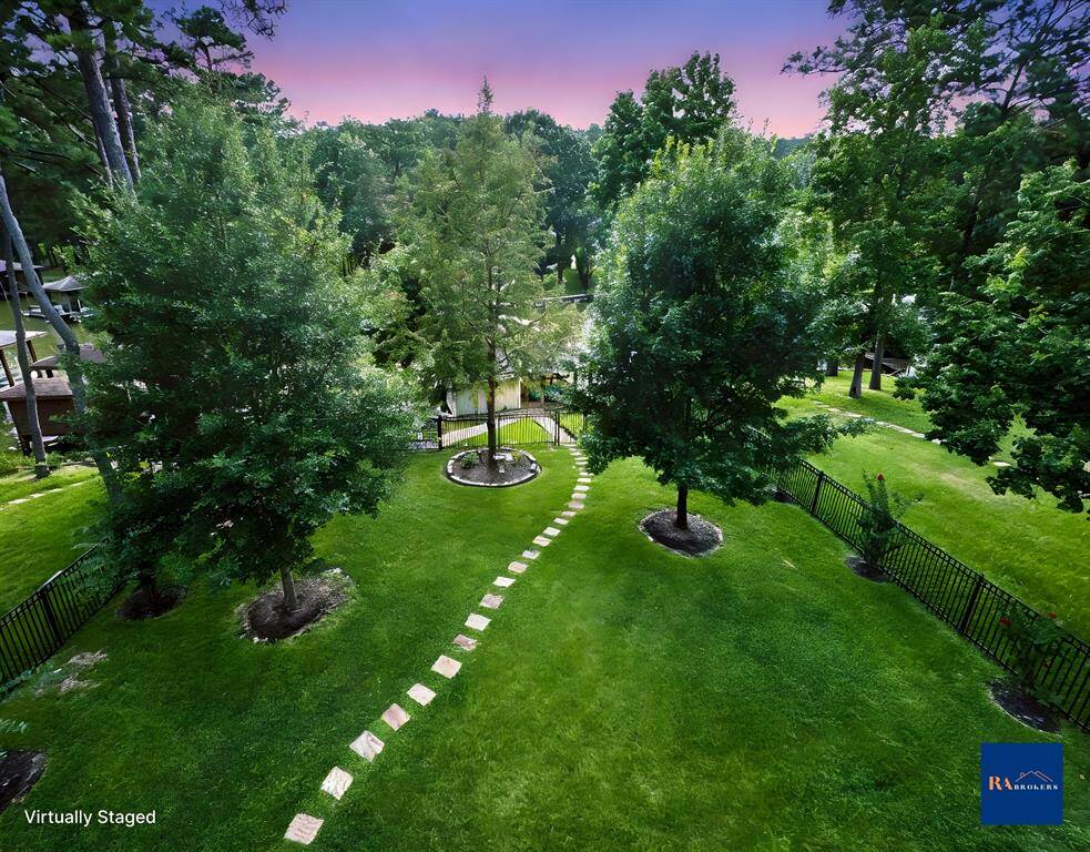 This photo showcases a spacious, lush backyard with a manicured lawn, mature trees, and a stone path leading to the boathouse.