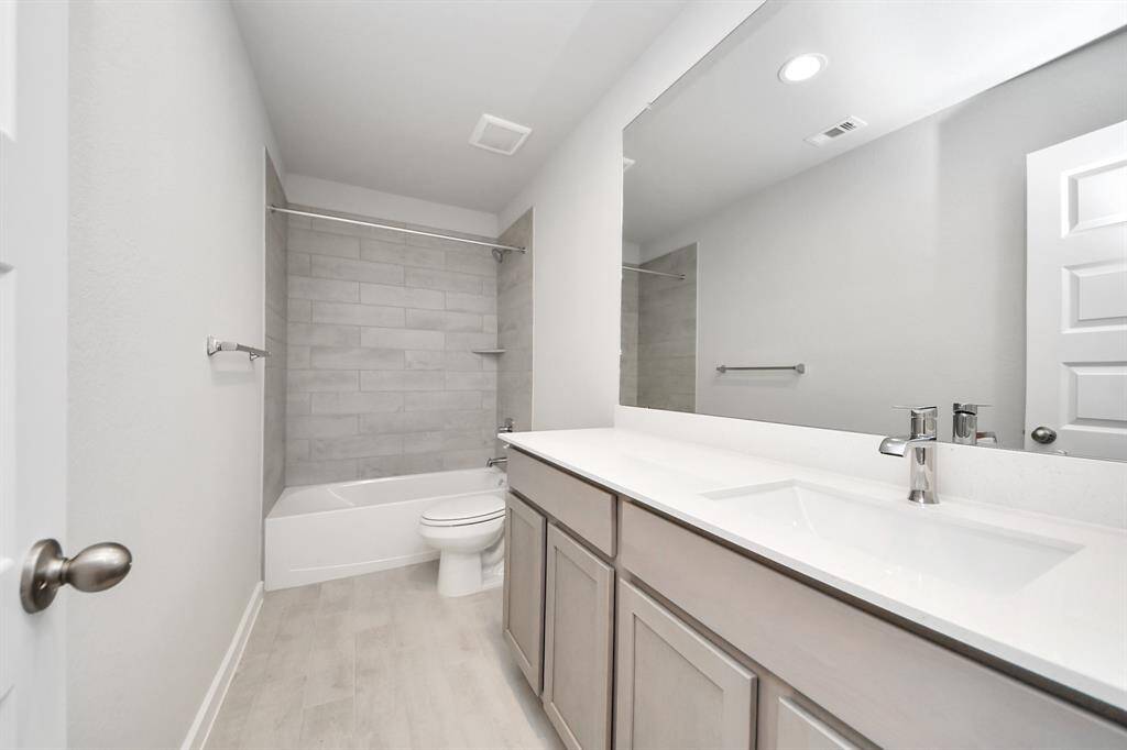 Secondary bath features tile flooring, bath/shower combo with tile surround, light stained wood cabinets, beautiful light countertop.