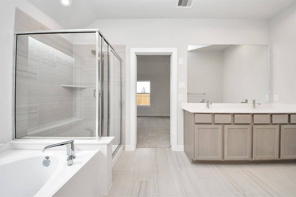 Escape to a spa-like oasis in this primary bathroom. Enjoy a walk-in shower with tile surround, a separate garden tub with custom detailing, and an elegant vanity featuring light countertops, modern hardware, and beautiful recessed lights. Experience luxury and relaxation in every detail