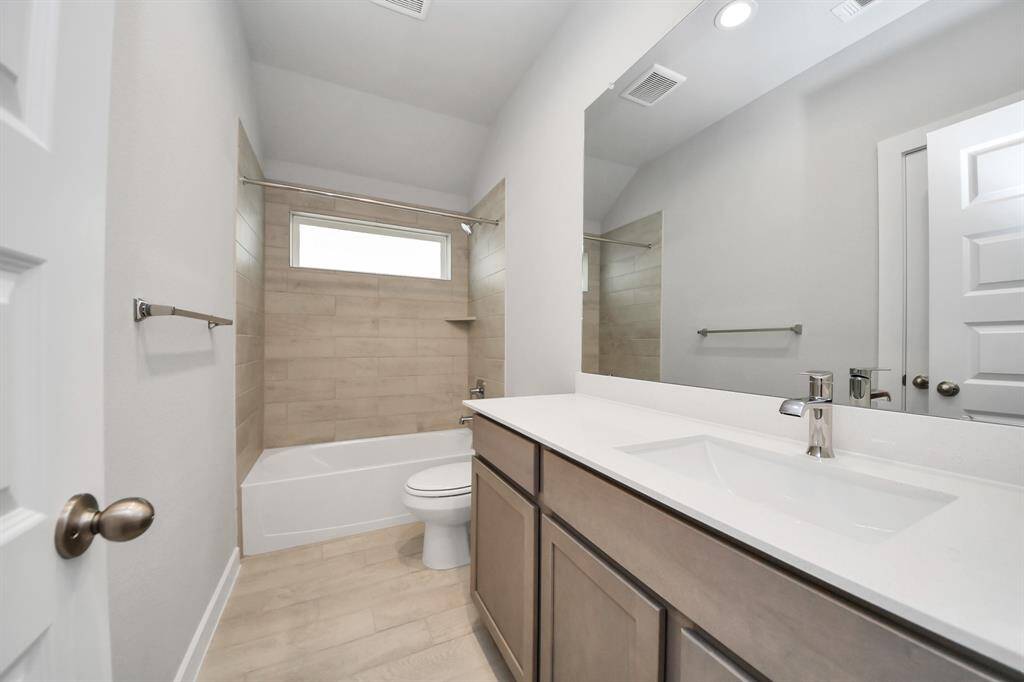 Secondary bath features tile flooring, bath/shower combo with tile surround, light stained wood cabinets, beautiful light countertop.