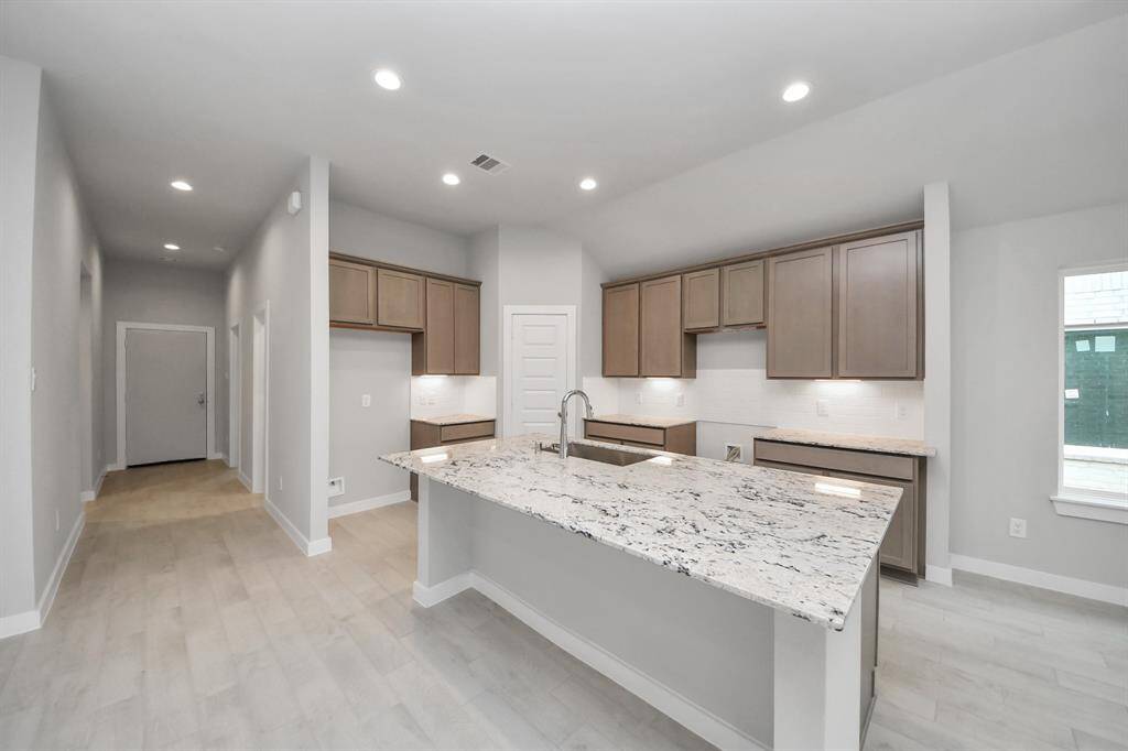 This generously spacious kitchen is a dream realized! With a massive granite island, high ceilings, soft close cabinets, granite countertops, stainless steel appliances, a sleek tile backsplash, recessed lighting, and an extended counter area.
