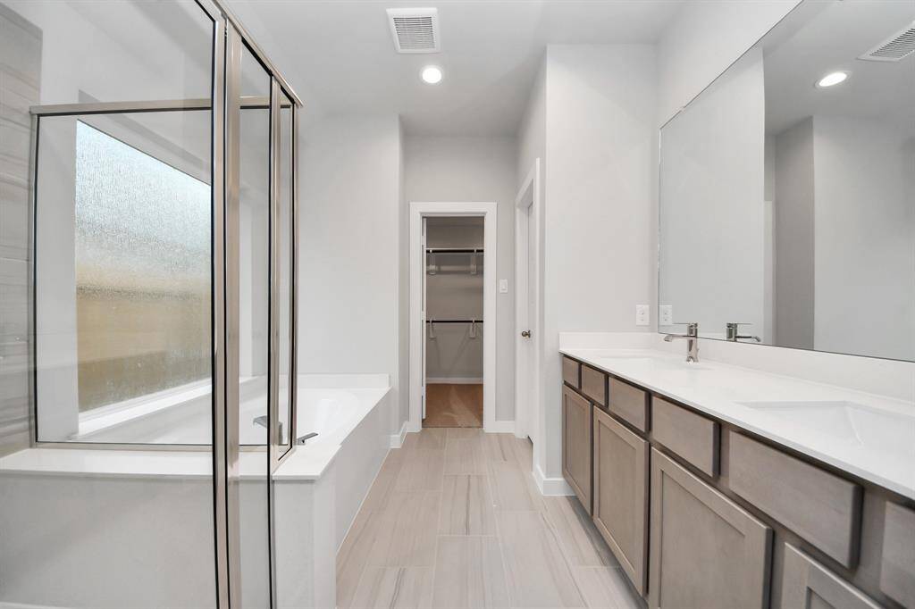 Escape to a spa-like oasis in this primary bathroom. Enjoy a walk-in shower with tile surround, a separate garden tub with custom detailing, and an elegant vanity featuring light countertops, modern hardware, and beautiful recessed lights. Experience luxury and relaxation in every detail