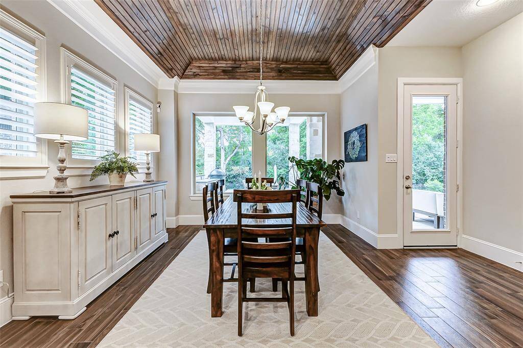The dining area is highlighted by an elegant lighting fixture above the table, drawing the eye upward to the custom tongue-and-groove wood ceiling. Large picture windows surround the space, flooding the room with natural light and offering picturesque views. This area also provides easy access to the expansive backyard, seamlessly extending your living space and enhancing the home’s indoor-outdoor flow.