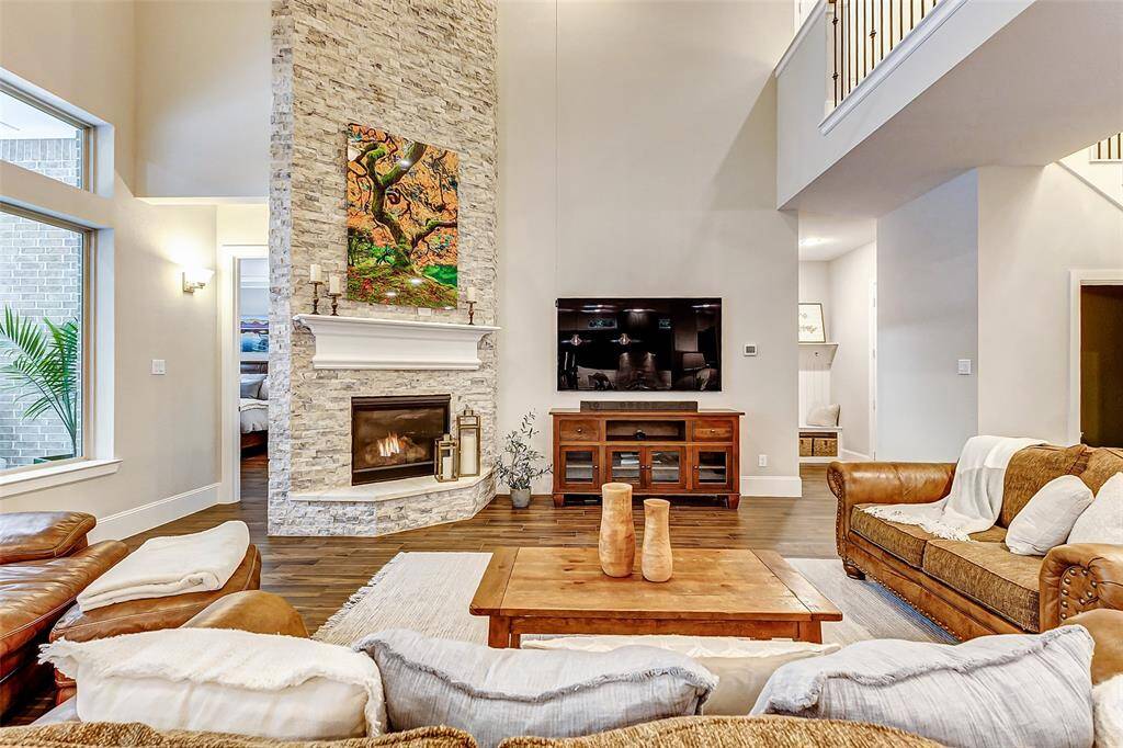 Welcome to this spacious and inviting living room, where a striking stacked stone fireplace makes a bold statement, extending all the way up to the soaring two-story ceiling.