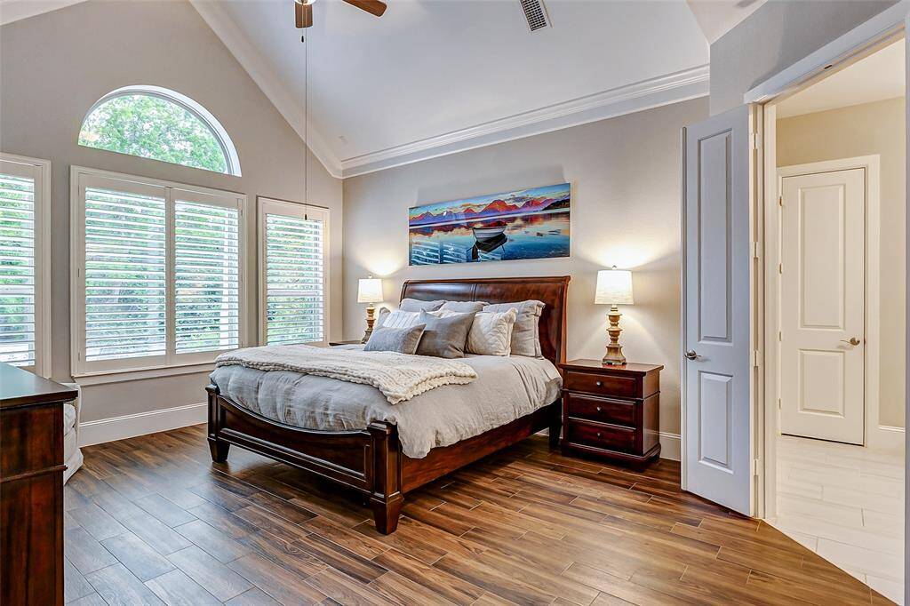 Retreat to your serene primary bedroom, featuring elegant tile flooring, a vaulted ceiling with crown molding, and large windows with plantation shutters that frame tranquil views of the wooded greenspace.