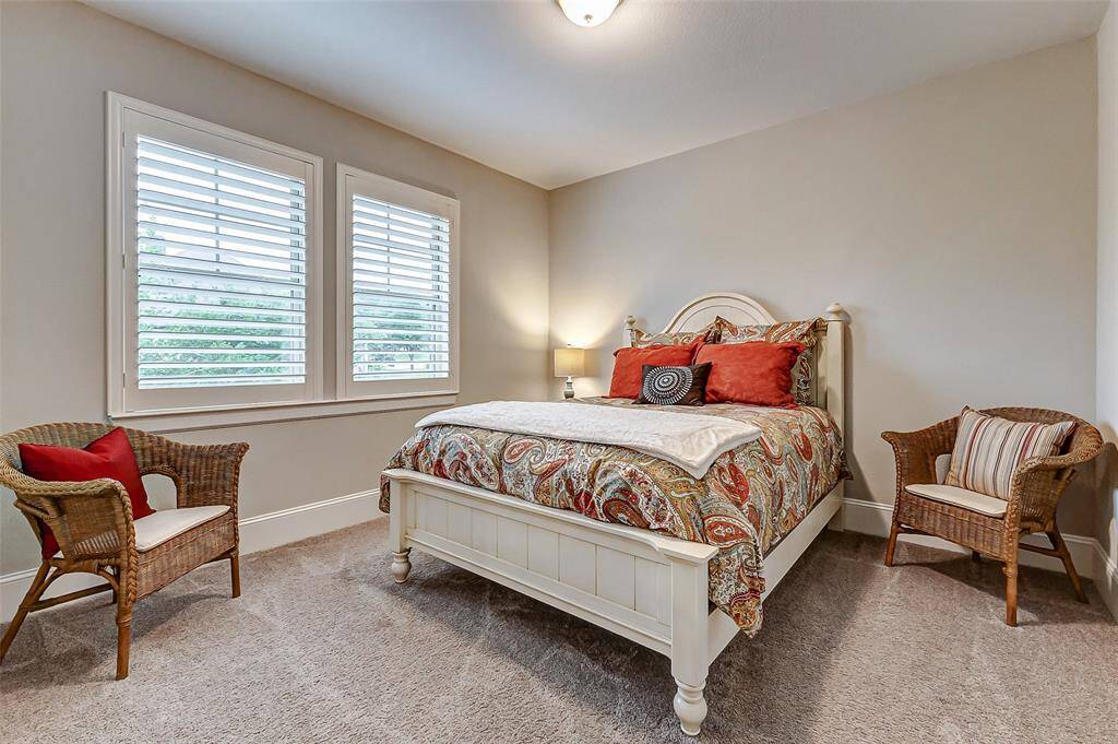 This upstairs secondary bedroom offers comfort and style with plush carpeting, thick baseboards, and decorator paint. The room also features a spacious closet and windows with classic plantation shutters, creating a warm and inviting space.