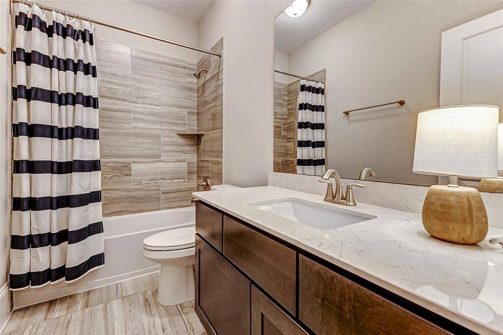 The upstairs full bathroom features a spacious vanity with stained cabinetry, sleek quartz countertops, and a tub/shower combination—offering both style and functionality for family or guests.