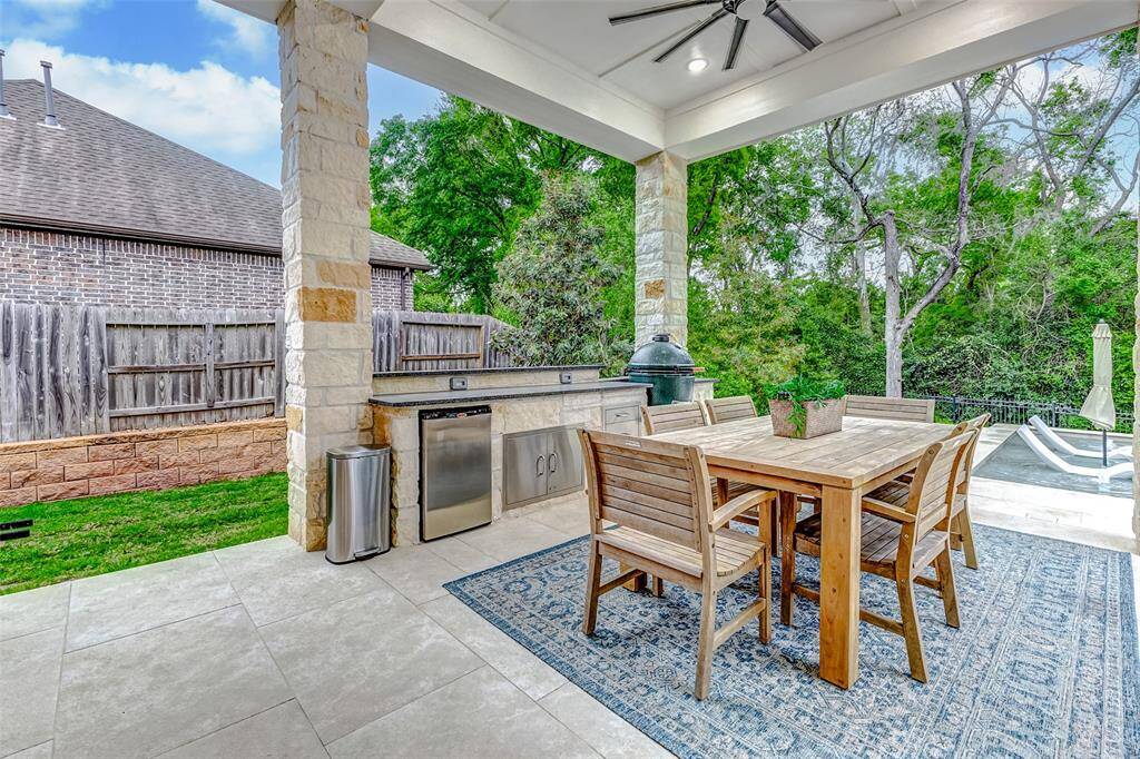 An alternate view of the custom patio reveals the well-appointed outdoor kitchen and dining area, all situated beneath a covered structure with a ceiling fan and stately stone pillars—offering the perfect blend of comfort and style for outdoor entertaining.