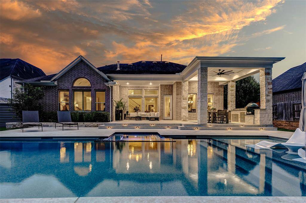Take note of the elegant travertine decking that surrounds the pool, offering both durability and style. Lighted steps lead gracefully up to the covered patio area, creating a warm and inviting transition from poolside relaxation to outdoor dining and entertaining.