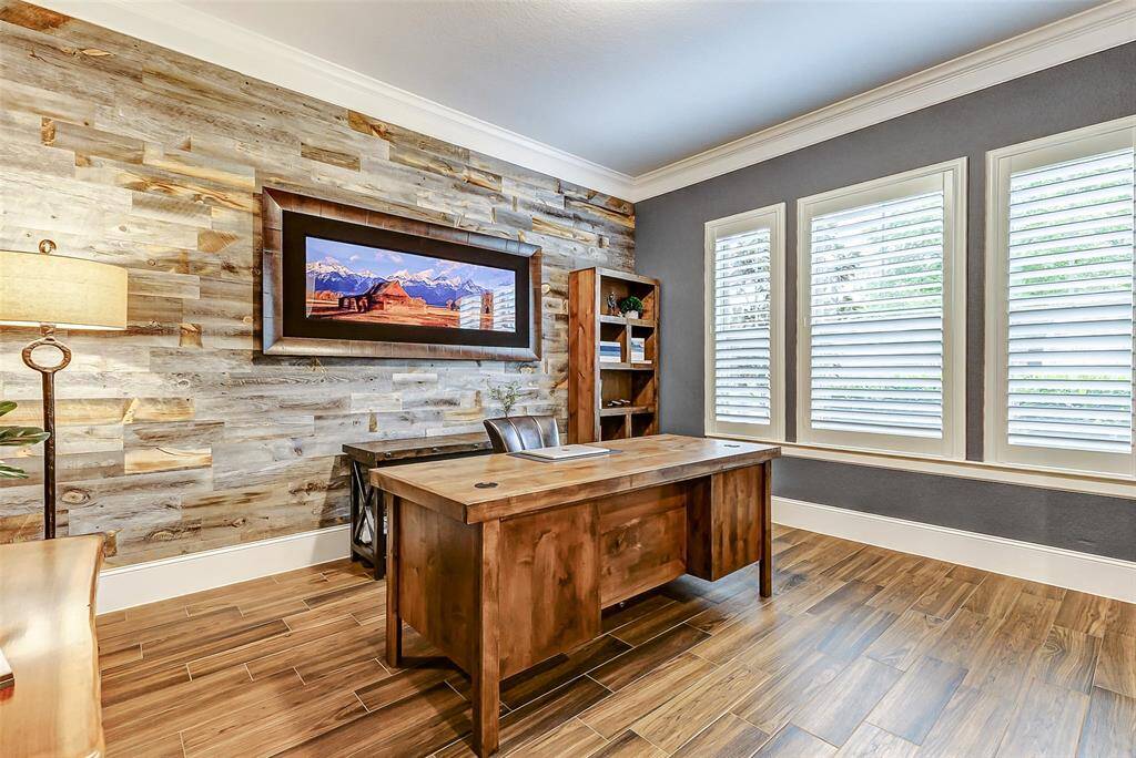 Enclosed by glass French doors, this stunning study offers a refined workspace featuring tile flooring, thick baseboards, elegant crown molding, and three large windows adorned with plantation shutters—filling the room with natural light and offering peaceful views of the front yard.