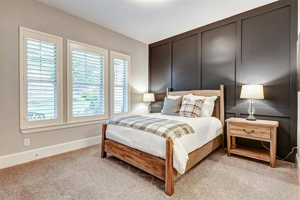 The downstairs guest bedroom features a striking board and batten accent wall that immediately draws the eye, adding charm and character to the space. Plush carpeting, thick baseboards, and three large windows with plantation shutters provide both comfort and style, along with serene views of the front yard.