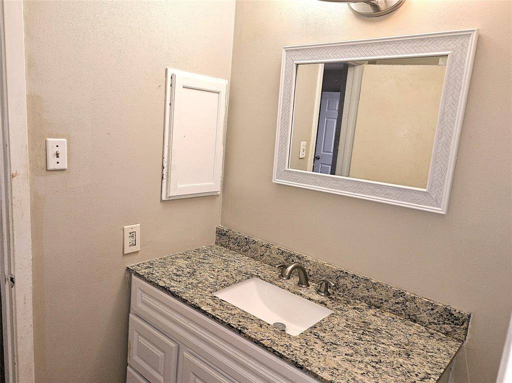 This bathroom features a granite look countertop with an undermount sink, a framed mirror, and neutral wall colors. There's a small, recessed cabinet for storage.