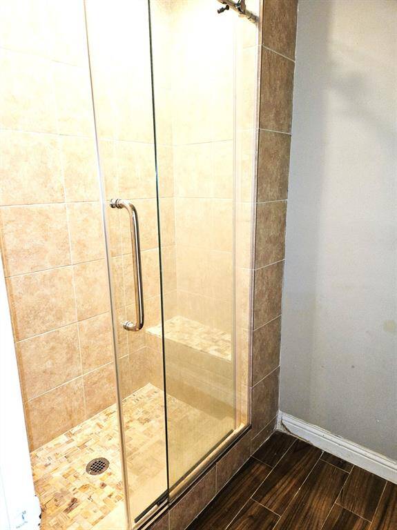 This photo shows a modern shower with a glass door and tiled interior. The shower features a built-in bench and is set against neutral-colored tiles, complemented by wood-look flooring outside.