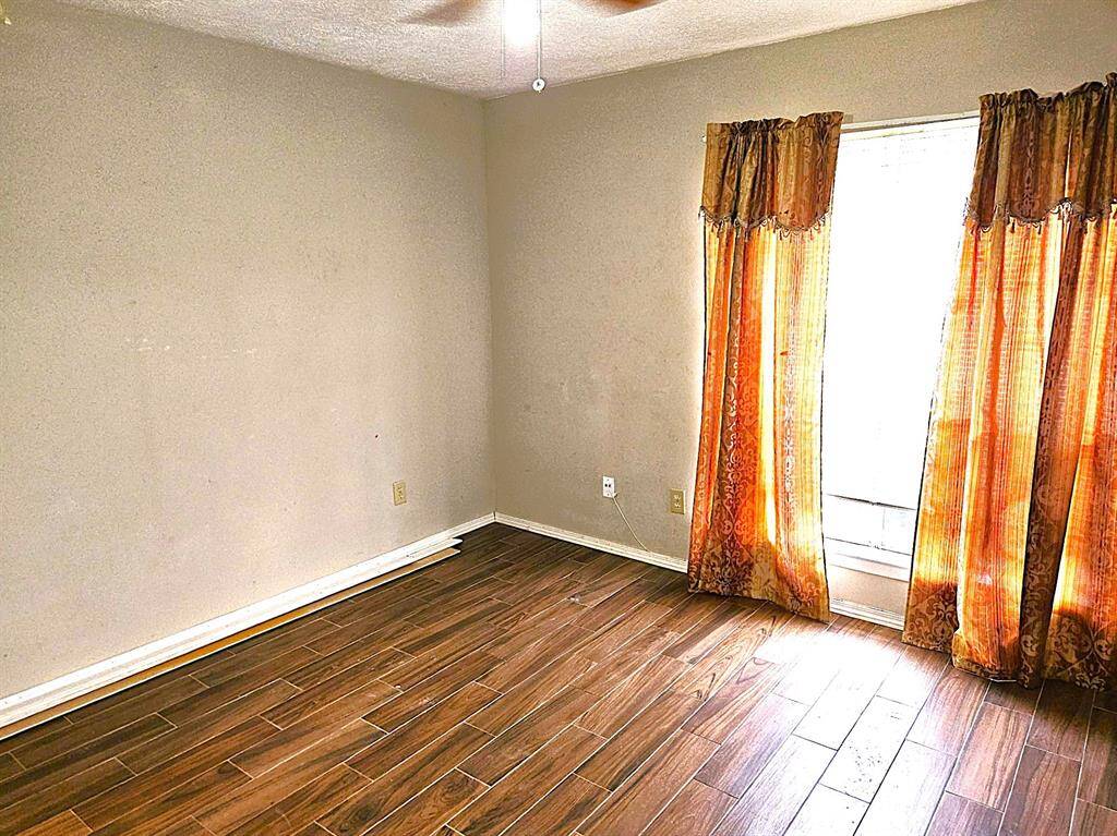 This room features wood-look tile flooring, neutral-colored walls, and a window with vibrant orange curtains, allowing natural light to fill the space.