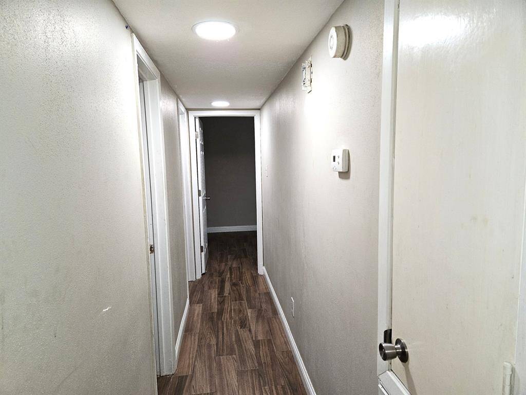 This photo shows a narrow, well-lit hallway with wood-look flooring and neutral walls, leading to multiple rooms.
