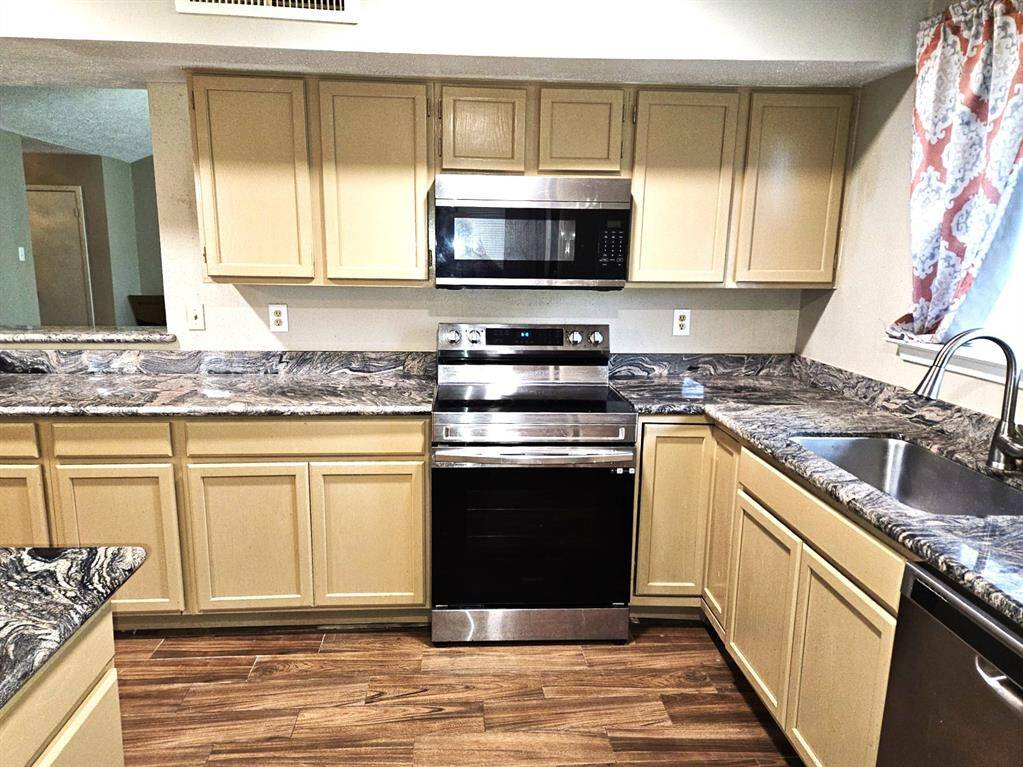 Modern kitchen featuring sleek stainless steel stove, disher washer and microwave and, ample cabinet storage, and elegant granite countertops. The space is brightened by a window above the sink, accented with patterned curtains.