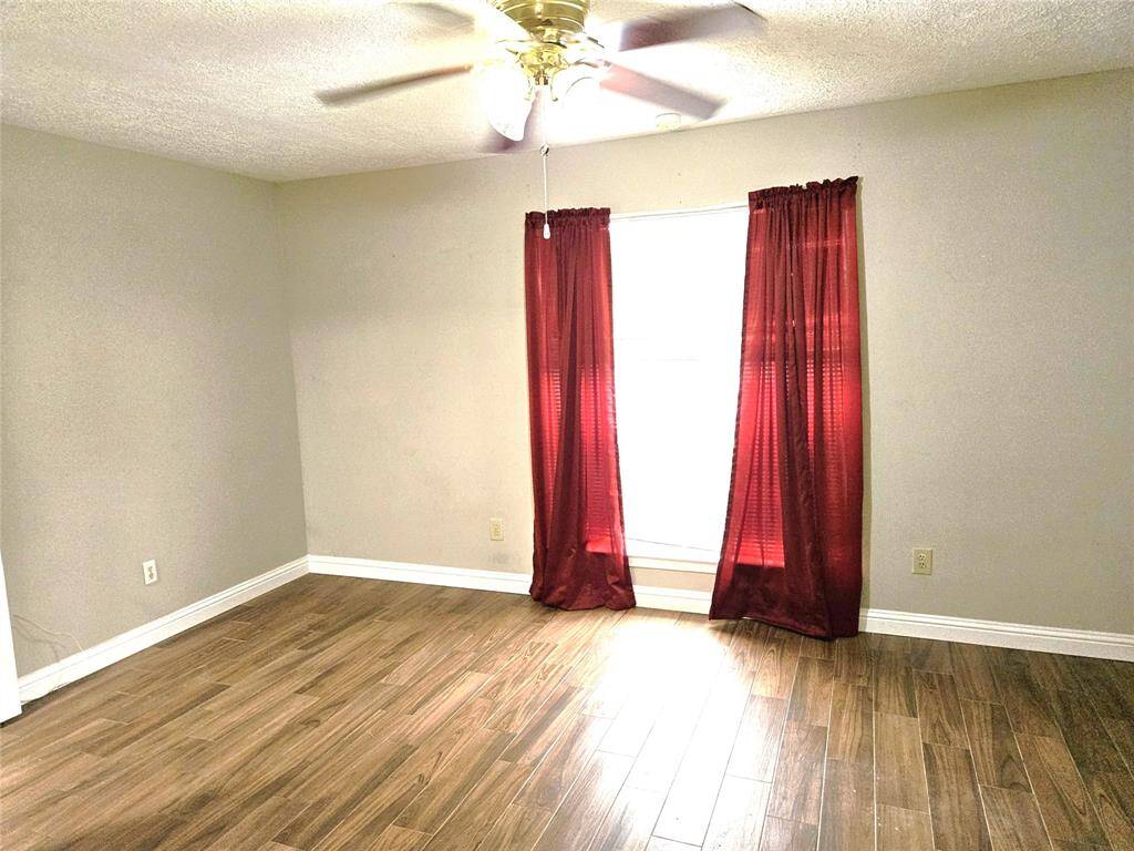 This room features tile wood flooring, neutral walls, and a ceiling fan. A window with beautiful red curtains allows natural light, creating a bright and inviting space.