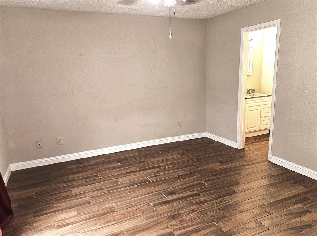This room features wood-look tile flooring, neutral walls, and a ceiling fan. There is an adjoining space with a vanity visible through an open doorway, suggesting a connection to a bathroom.