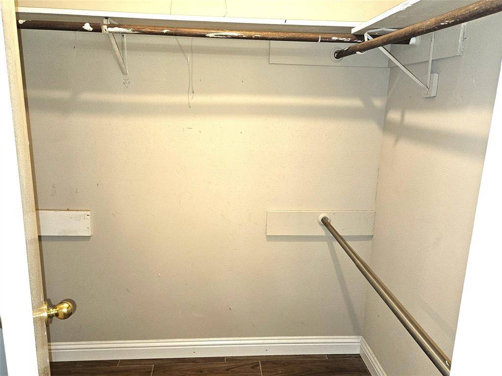 This photo shows a small walk-in closet with a wooden rod for hanging clothes, a shelf above, and a tile floor. The walls are a neutral color, providing a clean and simple storage space.