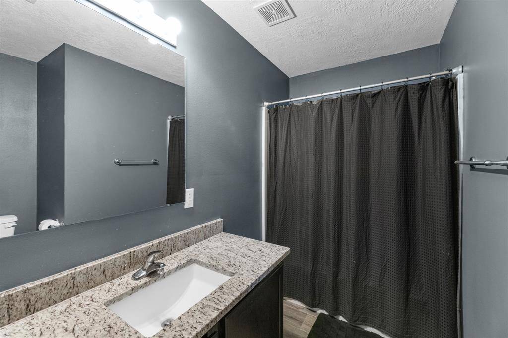 View of the primary bathroom with granite countertops and shower.