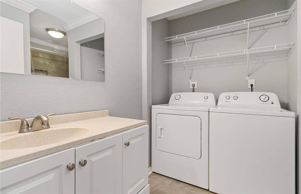 Laundry area features a sink with cabinets and hanging shelves providing ample storage for detergents, cleaning supplies, and other essentials, keeping everything neatly tucked away.