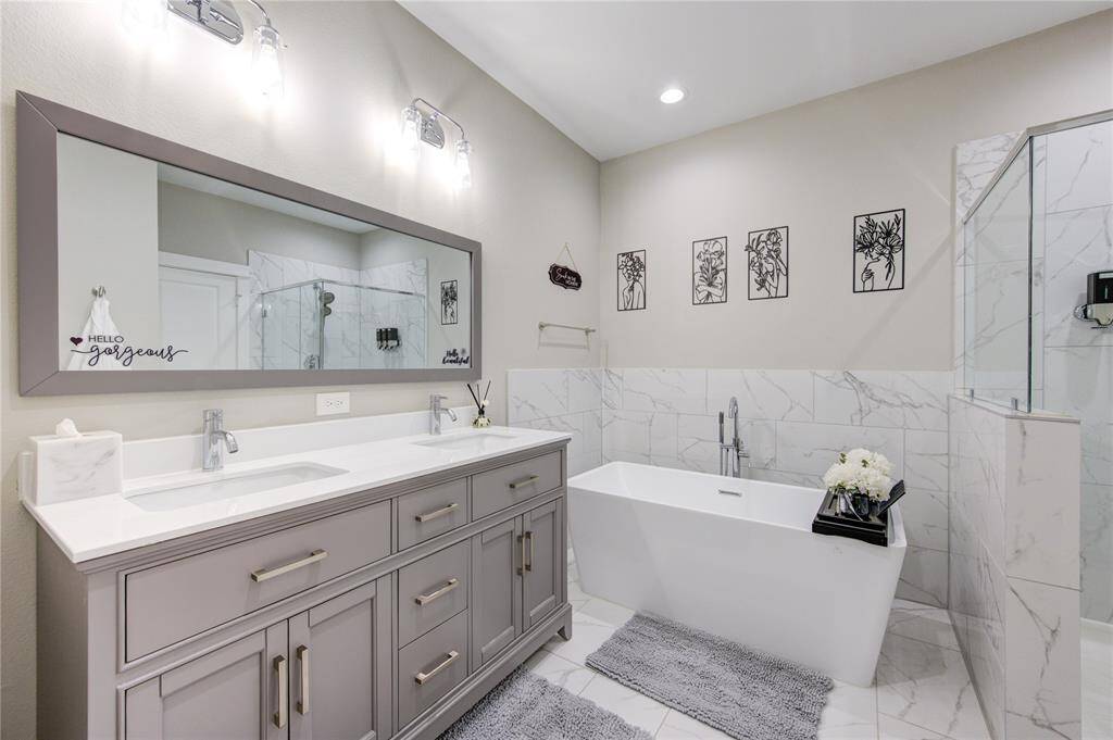 The space is accented by marble-style tiles and a double vanity with ample storage. Soft lighting and decorative wall art create a relaxing ambiance.