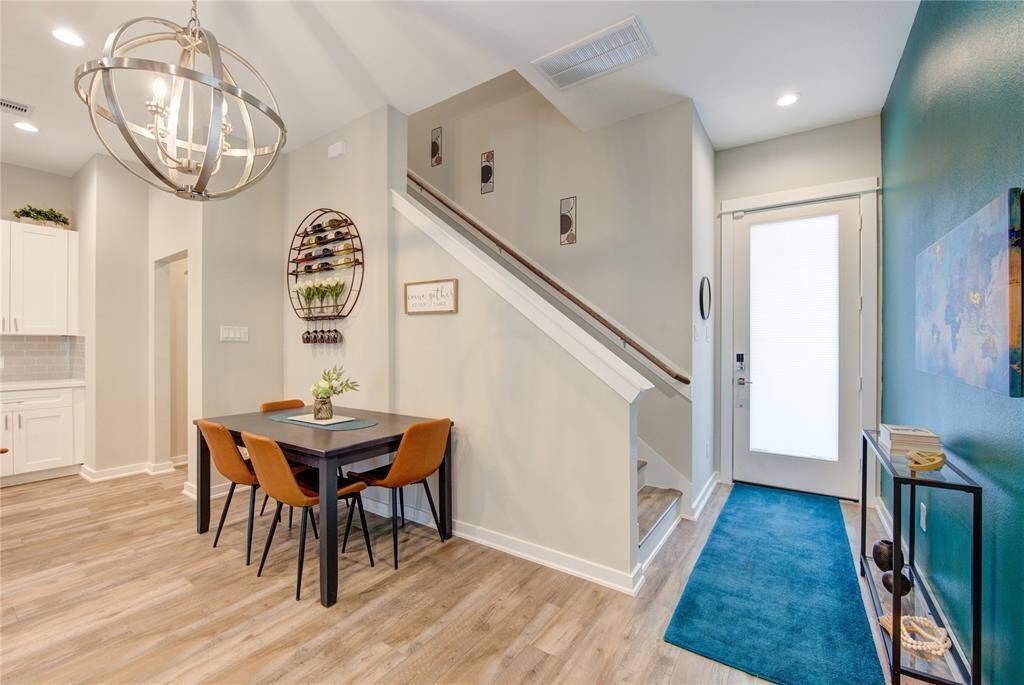 This inviting entryway features a modern dining area with a stylish chandelier, sleek wooden flooring, and a cozy staircase leading upstairs.