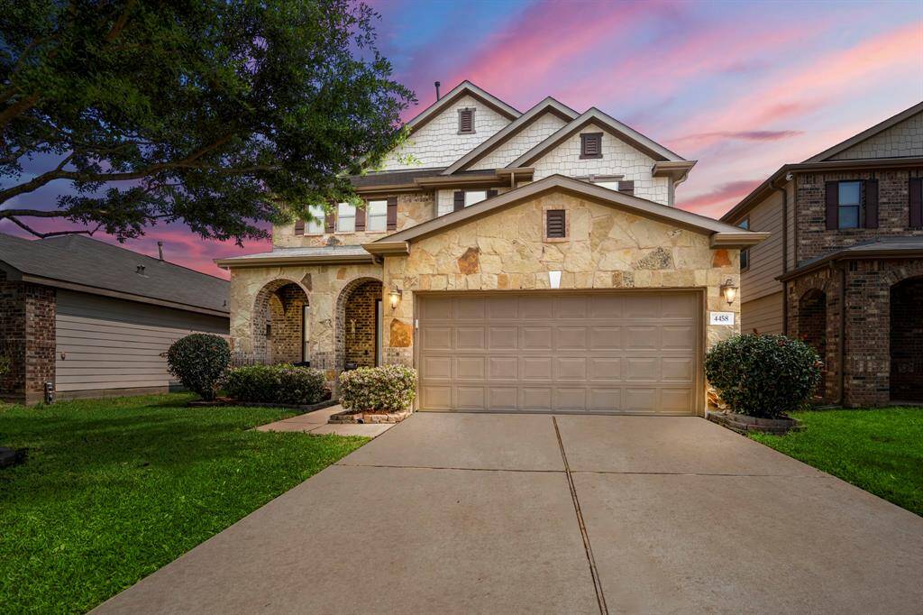 This inviting home features a stone facade with a two-car garage and a welcoming front porch. The well-maintained lawn enhances its curb appeal, set against a picturesque sunset sky. Perfect for families seeking a cozy neighborhood.