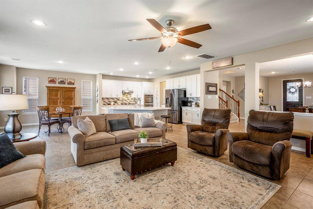 This spacious living area features an open-plan design with a cozy seating arrangement, a ceiling fan, and ample natural light. The connected kitchen boasts modern appliances and a breakfast bar. Neutral tones create a warm, inviting atmosphere.