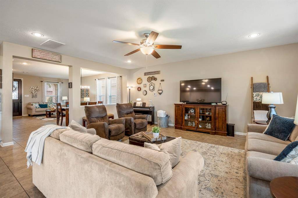 This spacious living room features neutral tones, comfortable seating, and a ceiling fan. Natural light fills the space through multiple windows.
