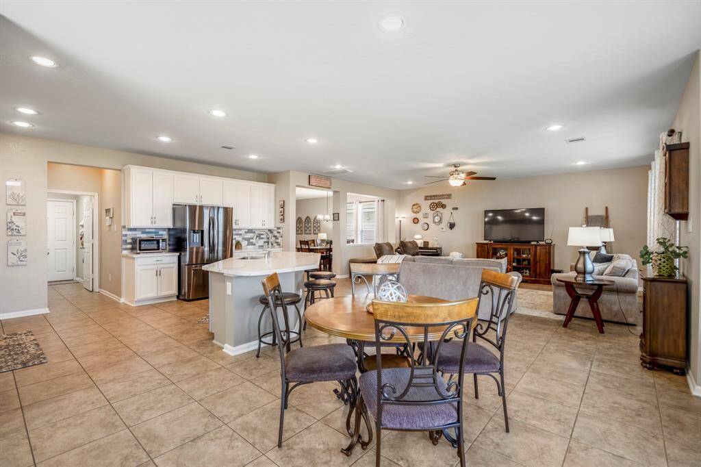 This spacious open-concept living area features a modern kitchen with white cabinetry, stainless steel appliances, and a central island with bar seating. The adjacent dining area and cozy living room seamlessly blend, enhanced by warm lighting and neutral tile flooring, creating a welcoming atmosphere perfect for entertaining.