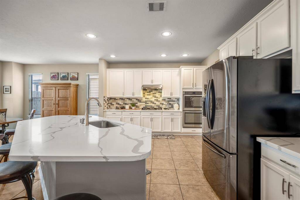 Spacious kitchen with modern design featuring a large marble island, stainless steel appliances, white cabinetry, and tile flooring. Natural light streams in through the windows, creating a bright and inviting atmosphere.